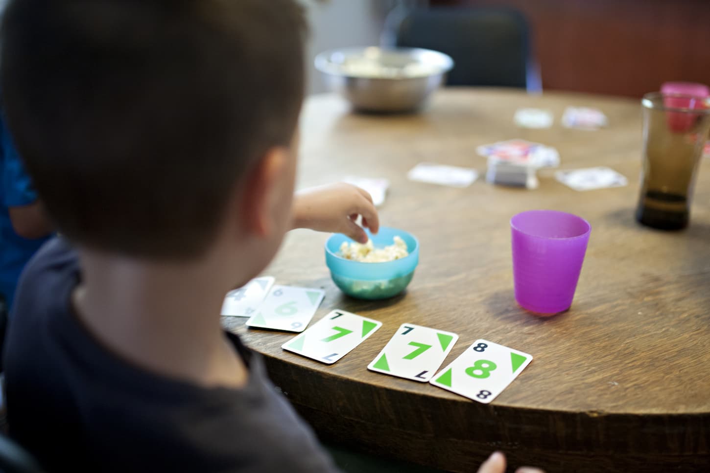 An image of a boy playing a card game while eating popcorn.