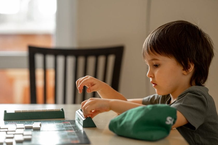 An image of The child sitting at the table and playing a board game. Playing words.