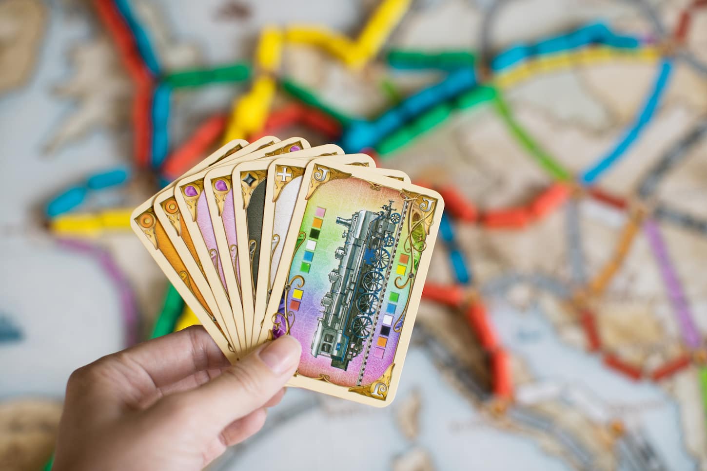 An image of a Hand holding cards of the Ticket to ride game, a railway-themed German-style board game.