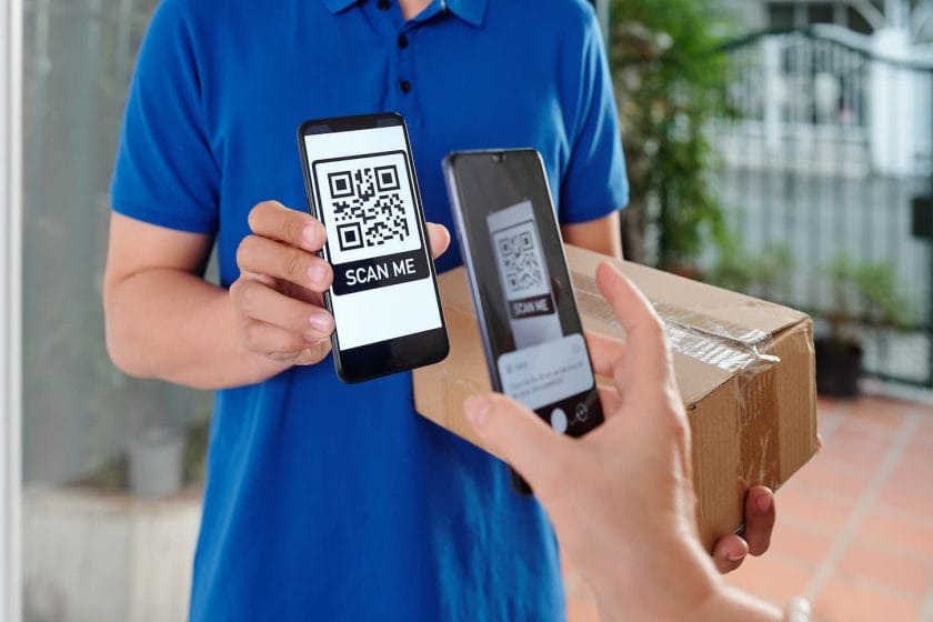 An image of a woman's hand scanning a QR code on a smartphone of a courier and paying for parcel delivery.