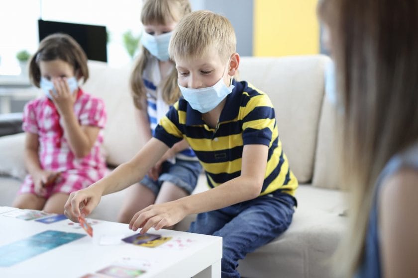 An image of Children in medical protective masks playing board games at home.