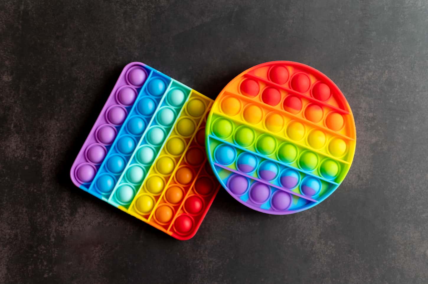 An image of kids anti stress sensory pop it or simple dimple fidget push toys on a black background.