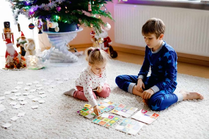 An image of Two little chilren, a cute toddler girl and a school kid boy playing together card game by a decorated Christmas tree. Happy healthy siblings, brother and sister having fun together.