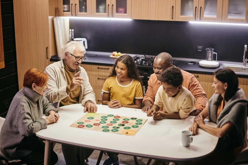 An image of a Large, happy multiracial family of three generations playing board games while sitting by a table in the kitchen.