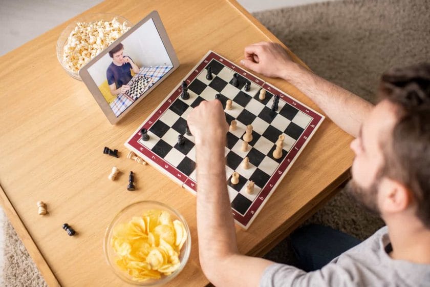 An image of a young man sitting at the coffee table and playing a chess game against an opponent online in home isolation.